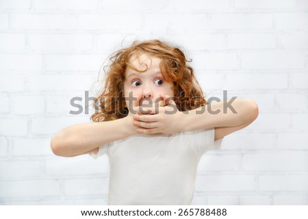 Little girl covering her mouth with her hands. Surprised or scared. On the light background indoors. Royalty-Free Stock Photo #265788488