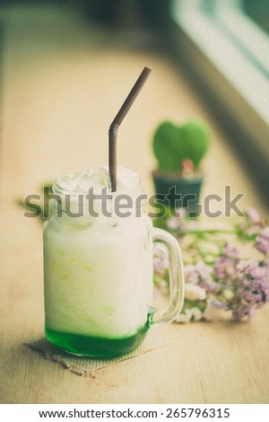 Fresh milk with green syrup on wood bar in cafe with film filter effect