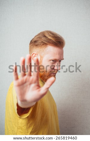 on a gray background man with a beard in the yellow shirt is outraged and shows stop