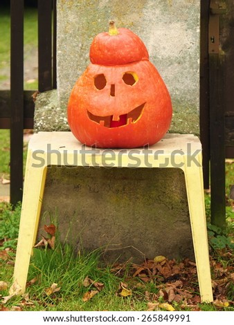 A close up shot of a happy jack-o-lantern sitting on a chair in front of house gate.