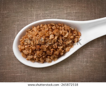 Buckwheat flakes in white porcelain spoon / high-res photo of grain in white porcelain spoon on burlap sackcloth background