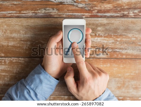 business, education, people and technology concept - close up of male hands holding smartphone with magnifying glass picture on screen at table