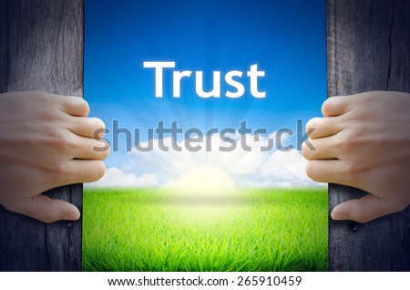 Trust. Hands opening a wooden door then found a texts floating among new world as green grass field, Blue sky and the Sunrise.