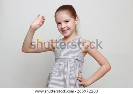 Attractive and cheerful little girl holding wooden heart symbol on holiday theme