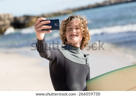 A surfer with his surfboard at the beach doing selfie