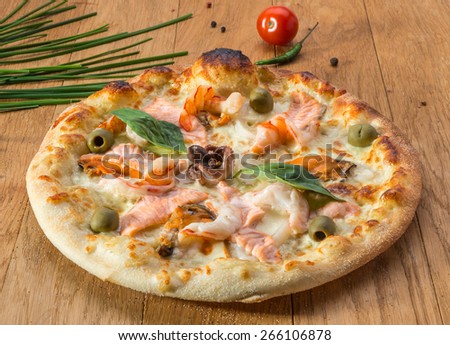 Delicious hot seafood pizza with shrimp, octopus, salmon, olives and different spices on wooden table ready to eat