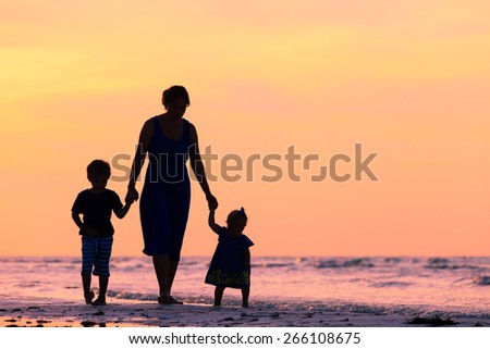 mother and two kids walking on sand beach at sunset