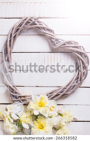 Fresh yellow daffodils and decorative  heart in ray of light  on white painted wooden planks. Selective focus. Place for text.