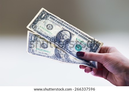 Two used one dollar banknotes in a woman's hand in a gradient background