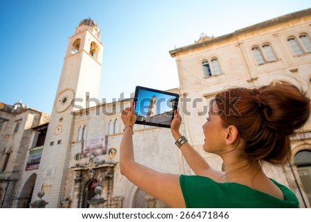 Young woman traveler photographing clock tower with digital tablet in Dubrovnik old city center.