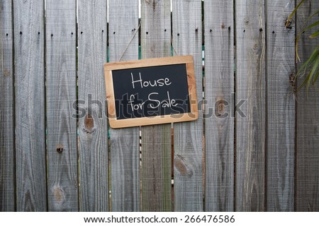 Blackboard home for sale sign on wooden fence