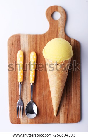 yellow passion fruit ice cream cone with spoon on wooden plate on white background