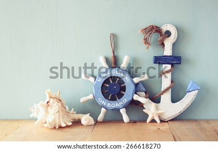 old nautical wood wheel, anchor and shells on wooden table over wooden background. vintage filtered image
