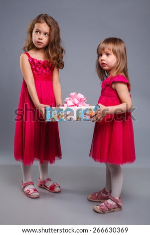 two little girls in beautiful dresses in the studio playing with a gift