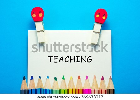 TEACHING word written on sticky note with clips and color pencils on blue background