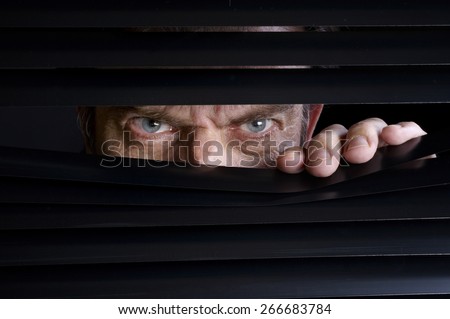 Man spying on something through venetian blinds Royalty-Free Stock Photo #266683784