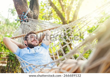 young caucasian man swinging in a hammock in a pleasant laziness of a weekend morning. He is smiling through his beard Royalty-Free Stock Photo #266689532
