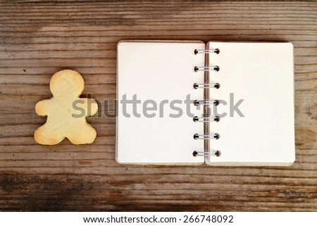 Homemade cookie in shape of man and empty retro spiral recipe book on wooden table