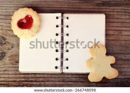Homemade cookies in shape of man and with heart shaped jam and empty retro spiral recipe book on wooden table