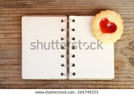 Homemade cookies with heart shaped jam and empty retro spiral recipe book on wooden table