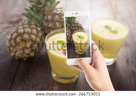 Taking photo of pineapple smoothie on wooden table.
