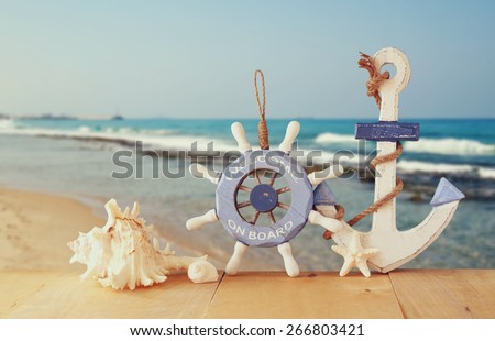 old nautical wood wheel, anchor and shells on wooden table over sea background.  