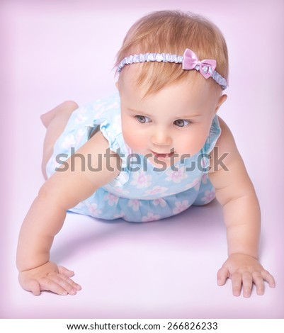 Cute little baby girl crawling in the studio on pink background, wearing nice dress and stylish head accessories, happy joyful childhood