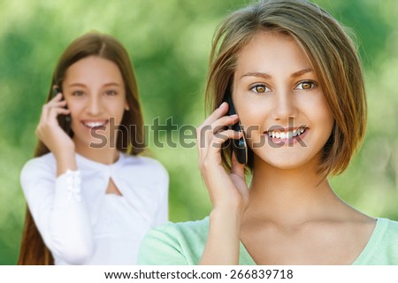 Beautiful smiling teenage girlstalking on mobile phone, against background of summer green park.