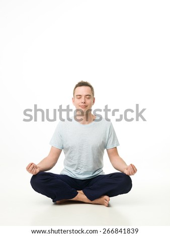 handsome caucasian man sitting in lotus position, meditating on white studio floor