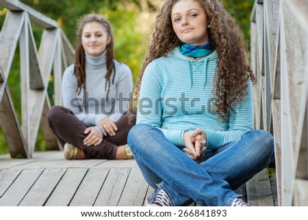Two young and beautiful girls at banisters of little bridge in city-park.