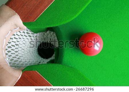 red billiard ball  in front of corner pocket on green baize table