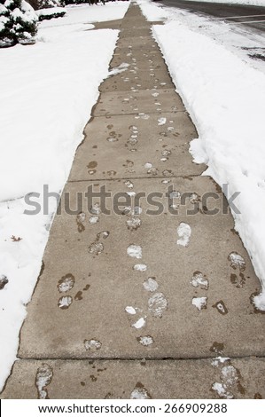 Footprints frozen in snow on long cement sidewalk