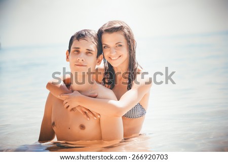 young beautiful girl embrace his boyfriend smiling in shallow water standing against azure sea and boat