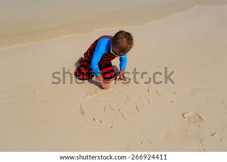 little boy drawing family picture on sand beach