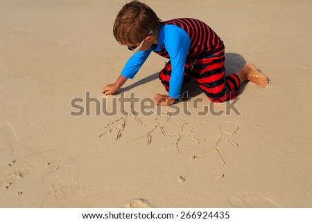 little boy drawing family picture on sand beach