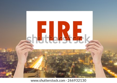 hands holding or showing white rectangle  with message FIRE  on blurred night city background,business text concept.