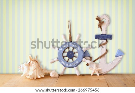 old nautical wood wheel, anchor and shells on wooden table over retro  background 