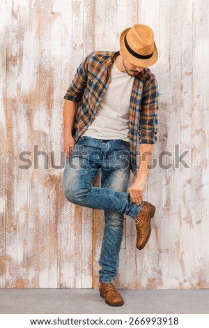 Everything should be perfect. Full length of handsome young man adjusting his jeans while standing against the wooden wall 