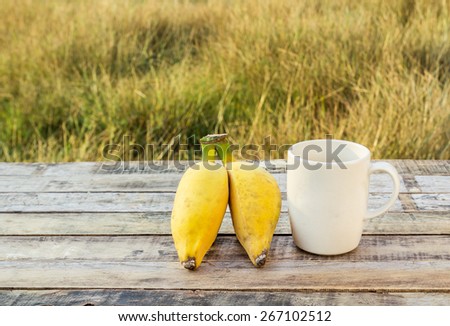 Ripe bananas and coffee cup on the wooden table outdoors with morning sunlight