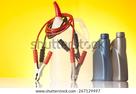 Car accessories - car liquid with jump start cables and plastic bottles of engine oil on yellow background