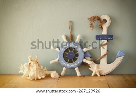 old nautical wood wheel, anchor and shells on wooden table over wooden aqua  background 