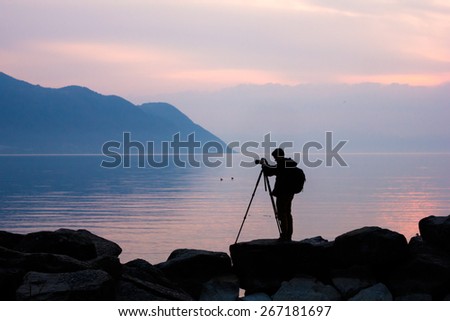 Silhouette of a professional photographer using a tripod, taking a photo of a mountain landscape