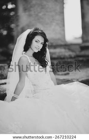 Black and white picture of happy bride wearing wedding dress and posing on steps of old church. 