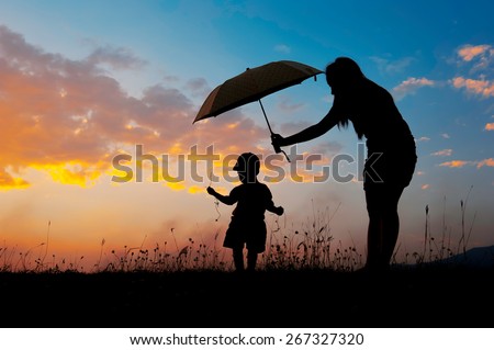 Silhouette of a mother and son holding umbrella and playing outdoors at sunset silhouette