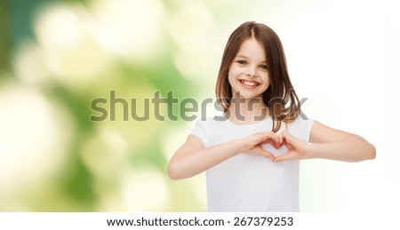 advertising, childhood, ecology, charity and people - smiling little girl in white t-shirt making heart-shape gesture over green background Royalty-Free Stock Photo #267379253