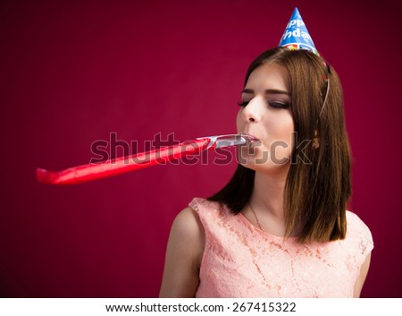 Young woman blowing in party whistle over pink background. Celebrating birthday.