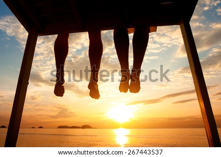 silhouette of feet of couple sitting on the pier at sunset beach, low angle view Royalty-Free Stock Photo #267443537