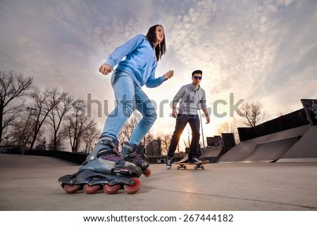 Girl on rollerblades and boy on skateboard in skate park