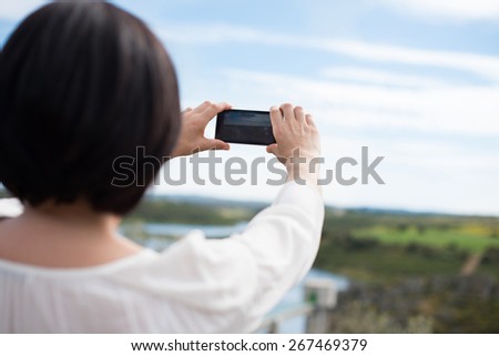 Back view of a woman taking photograph with a smart phone camera