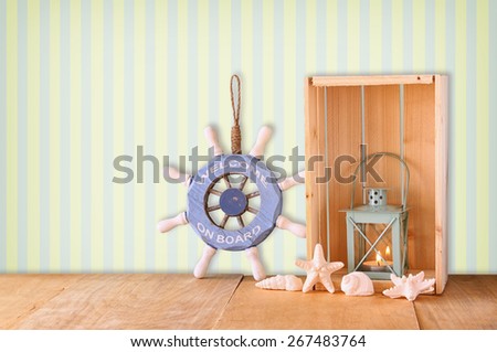 old nautical wood wheel, anchor and shells on wooden table over retro background
